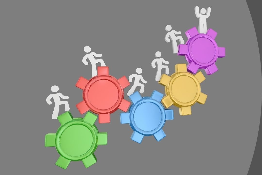 Photo of 5 gears each of which is a different colour and has figures climbing up them | featured image for Award Increase Blog for Bramwell Partners.