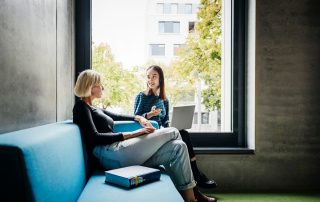 Two colleagues having a discussion on a couch | Featured image for the Employee Performance Management blog by Bramwell Partners.