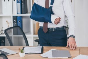 Man standing next to a desk with his arm in a cast and sling | Featured image for the When the Injury Is Not the Problem: Why Some Claims Turn into Long-Term Issues blog.